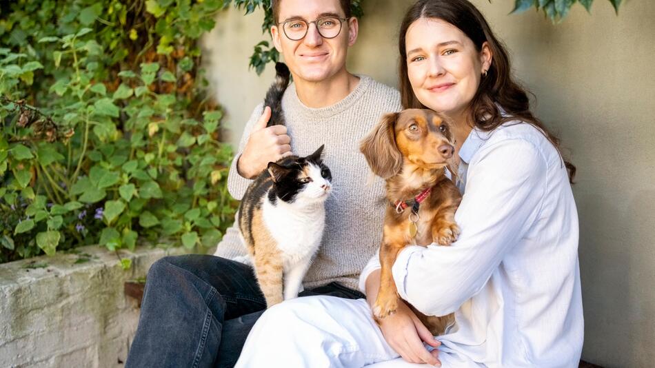 Ein Mann und eine Frau mit einer Katze und einem Hund auf dem Arm.