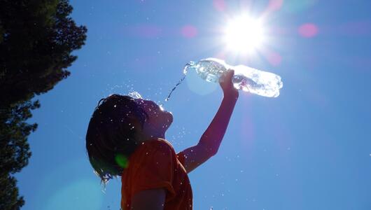 Kind kippt sich Wasser über den Kopf, die Sonne steht hoch am Himmel
