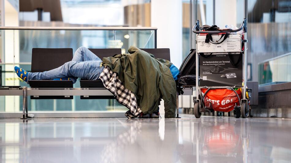 Mann schläft am Münchner Flughafen auf einer Sitzbank