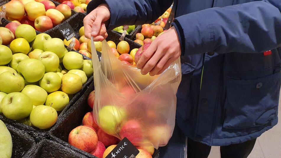 Mann hält eine dünne Plastiktüte, in der Obst liegt.