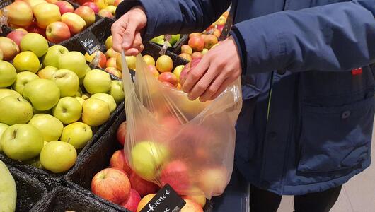 Mann hält eine dünne Plastiktüte, in der Obst liegt.