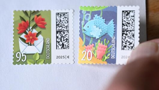Person klebt Briefmarke auf Briefumschlag