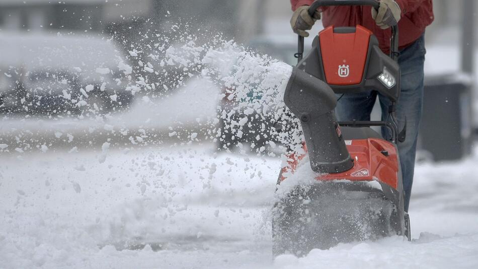 Mann räumt mit Hilfe einer Schneefräse den Gehweg