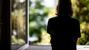 Eine junge Frau steht in ihrer Wohnung an einem Fenster