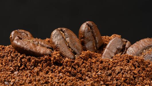 Geröstete ganze Kaffeebohnen liegen auf einem Haufen grob gemahlenem Kaffee.