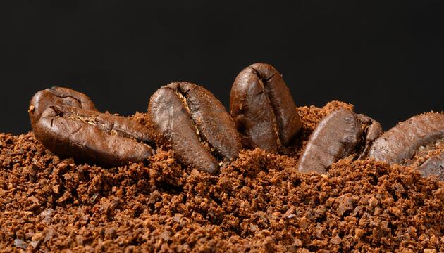 Geröstete ganze Kaffeebohnen liegen auf einem Haufen grob gemahlenem Kaffee.
