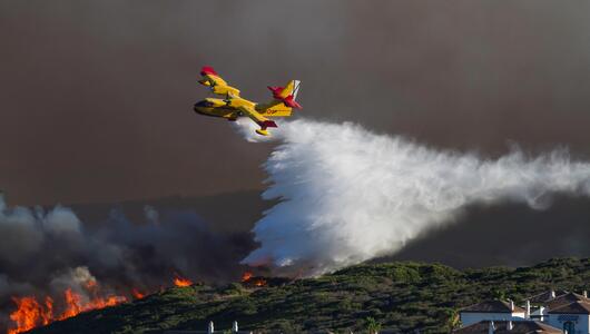 Löschflugzeug über brennendem Wald in Spanien