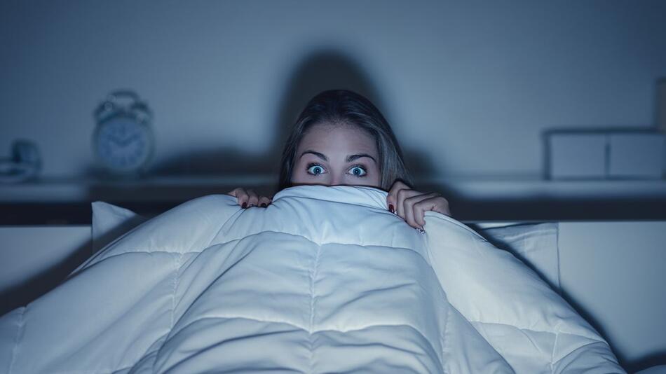 Frau fürchtet sich im Bett vor Horrorfilm.