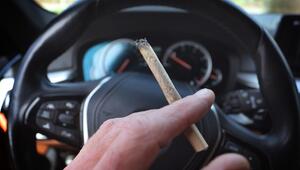 Mann sitzt mit einem Joint zwischen den Fingern am Steuer eines Autos