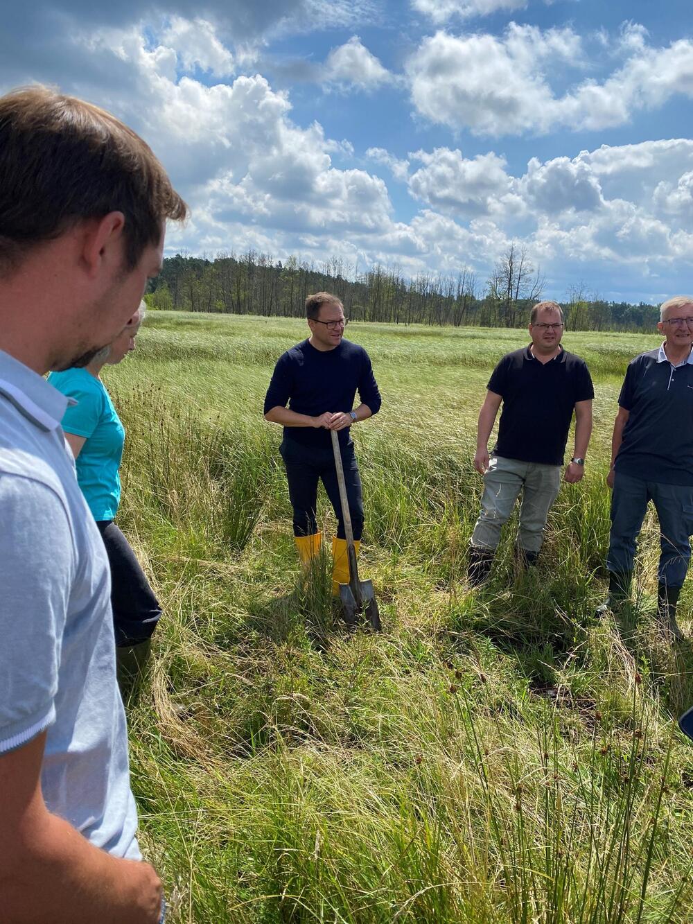 Umweltminister Schneider in gelben Gummistiefeln und mit Spaten auf einer Moor-Weide.