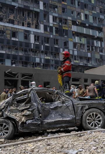 Ein Feuerwehmann steht auf einem verbrannten Auto vor einem zerstörten Gebäude.