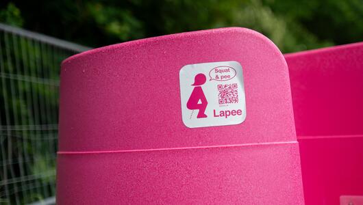 Knallpinkes Frauenpissoir mit „Squat & pee – Lapee“-Sticker bei Rock im Park 2025