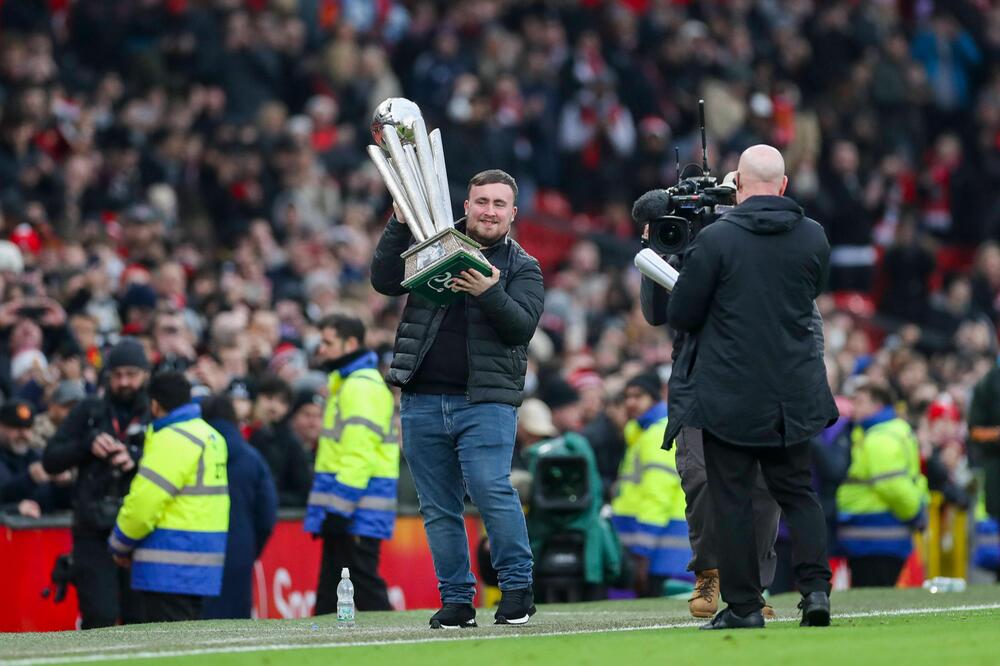 Darts-Weltmeister Luke Littler mit seiner Trophäe im Old Trafford