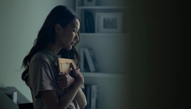 Junge Frau drückt einen Bilderrahmen an sich, sie hält sie Augen geschlossen