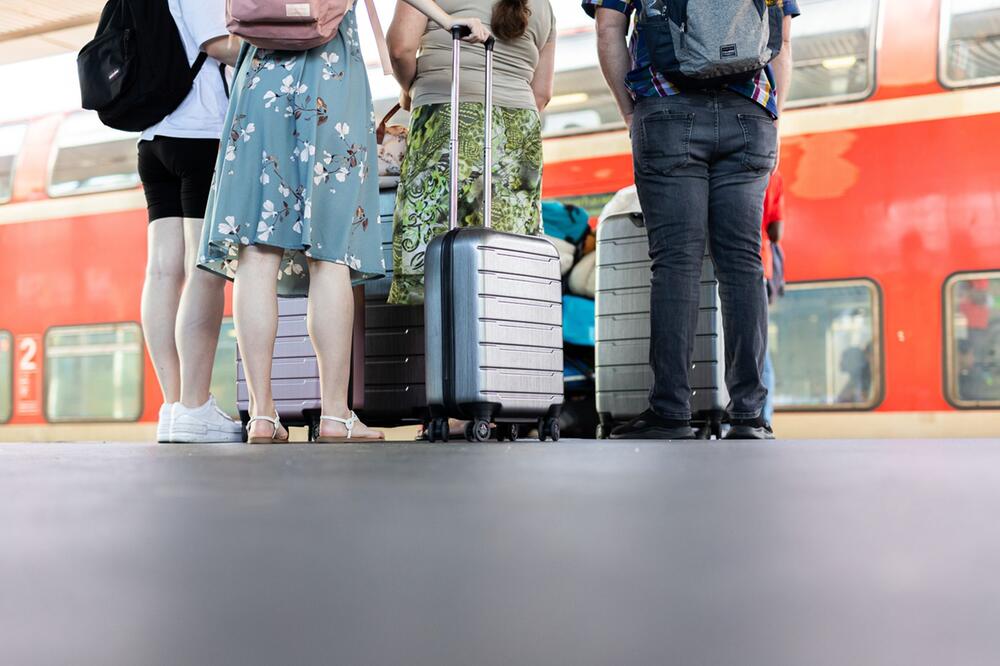 Personen stehen mit Koffern auf einem Bahnsteig