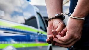 Eine Person steht in Handschellen gefesselt neben einem Polizeifahrzeug
