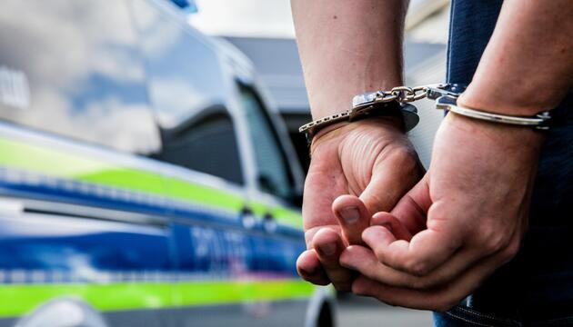 Eine Person steht in Handschellen gefesselt neben einem Polizeifahrzeug
