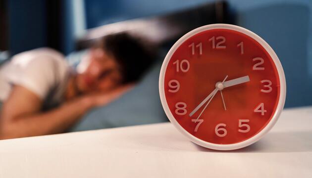 Mensch liegt im Bett, davor ein Wecker, dessen Uhrzeit auf 2:37 Uhr steht