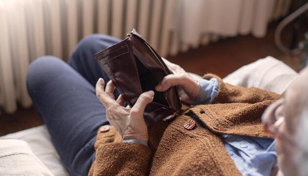 Ältere Person auf dem Sofa mit leerem Portemonnaie