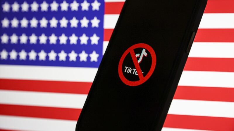 Ein Smartphone mit dem TikTok-Logo steht vor der USA-Flagge.