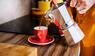 Frau gießt Kaffee in eine rote Tasse