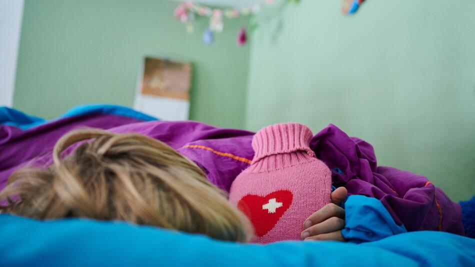 Ein Kind liegt mit Wärmflasche im Bett