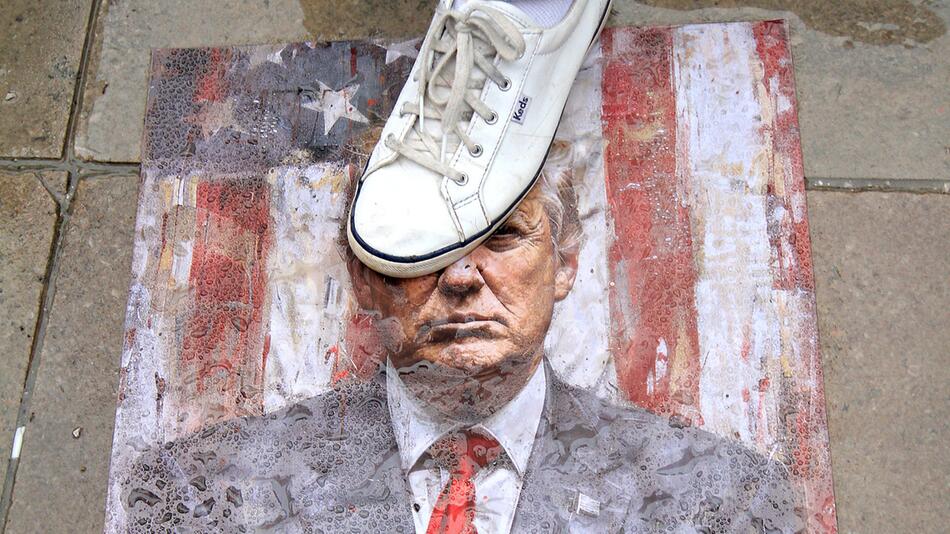 Ein Teilnehmer einer Demonstration steht auf einem Bild des US-Präsidenten Donald Trumps.